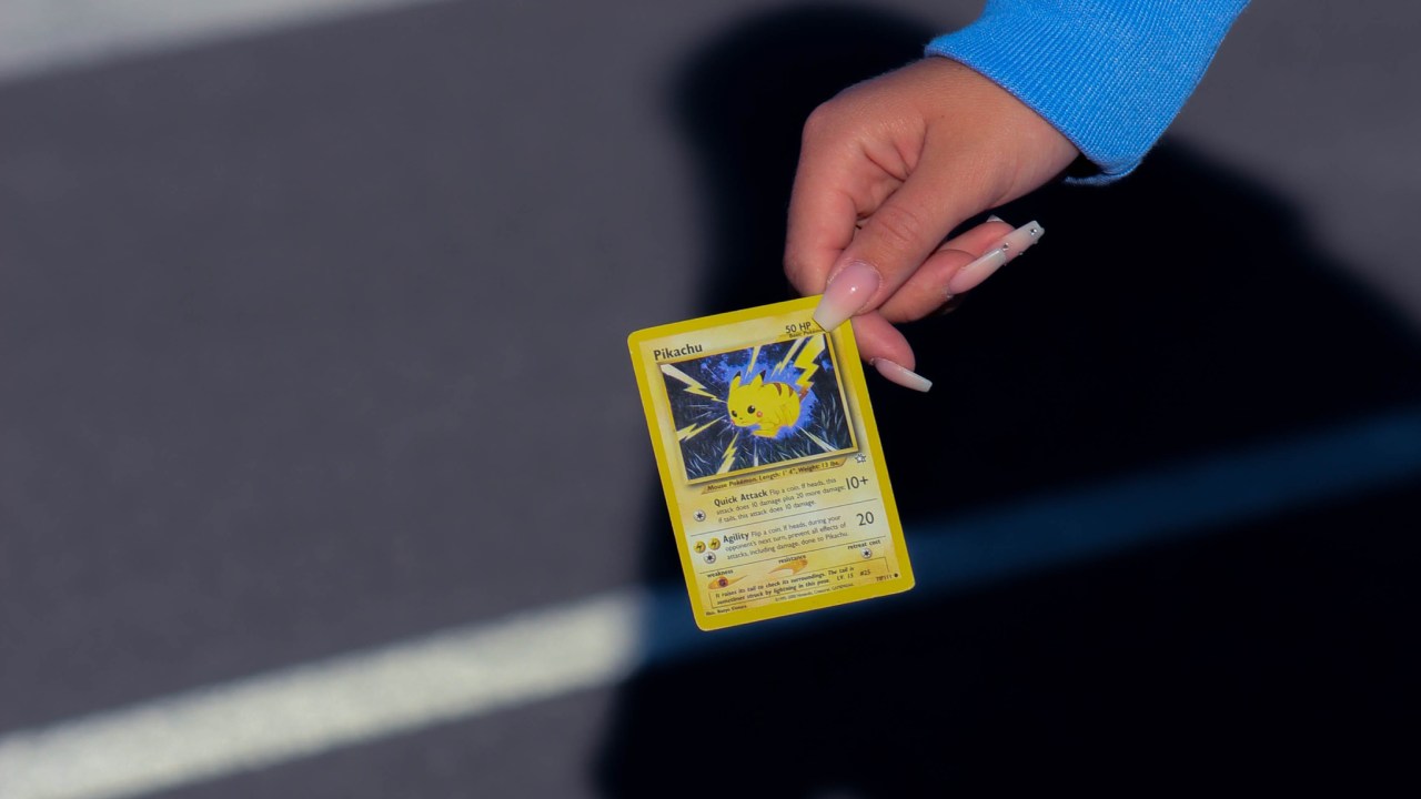 A hand holding a Pokémon card with a Pikachu on it.